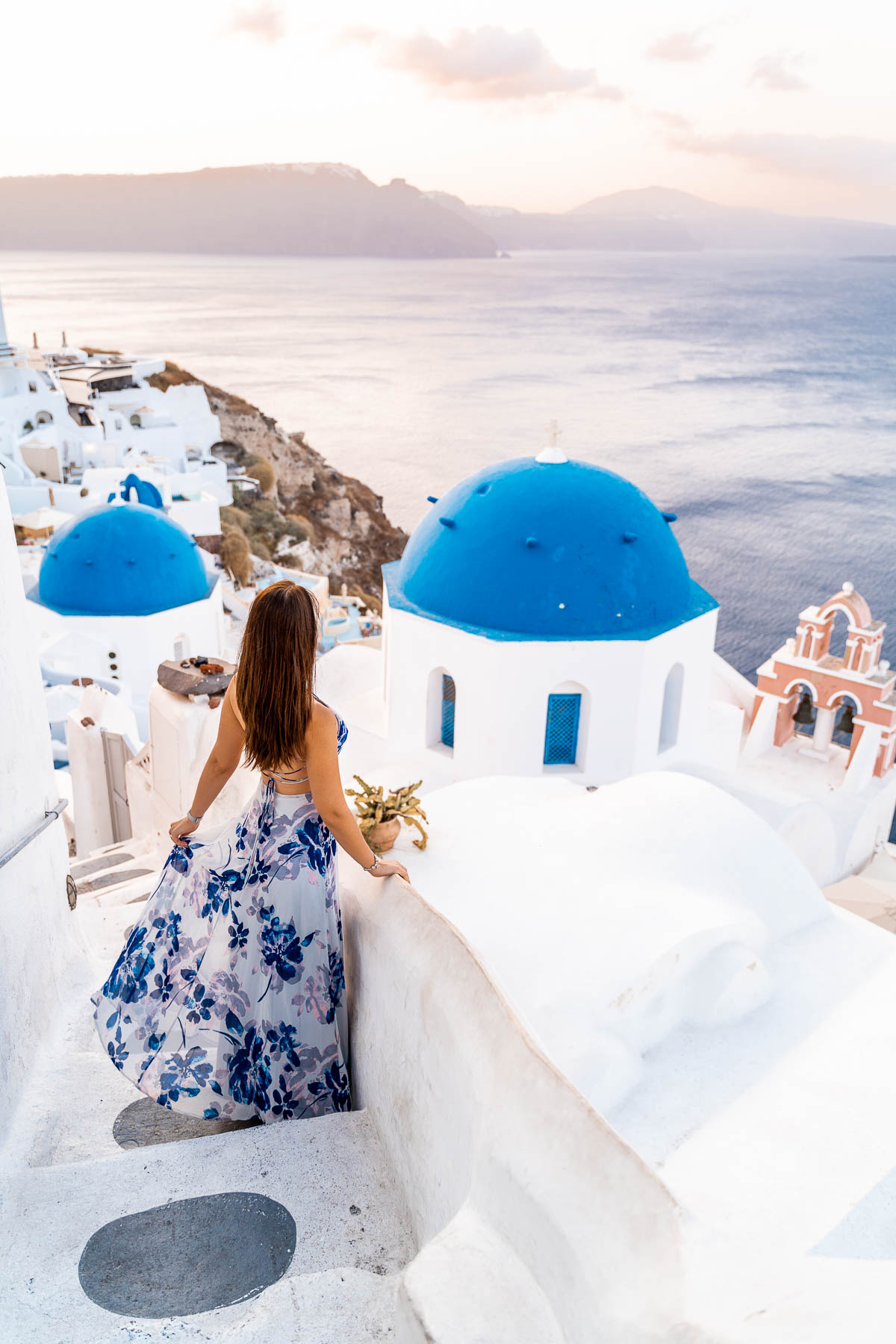 Girl in a blue dress standing in front of the three domes in Oia, Santorini