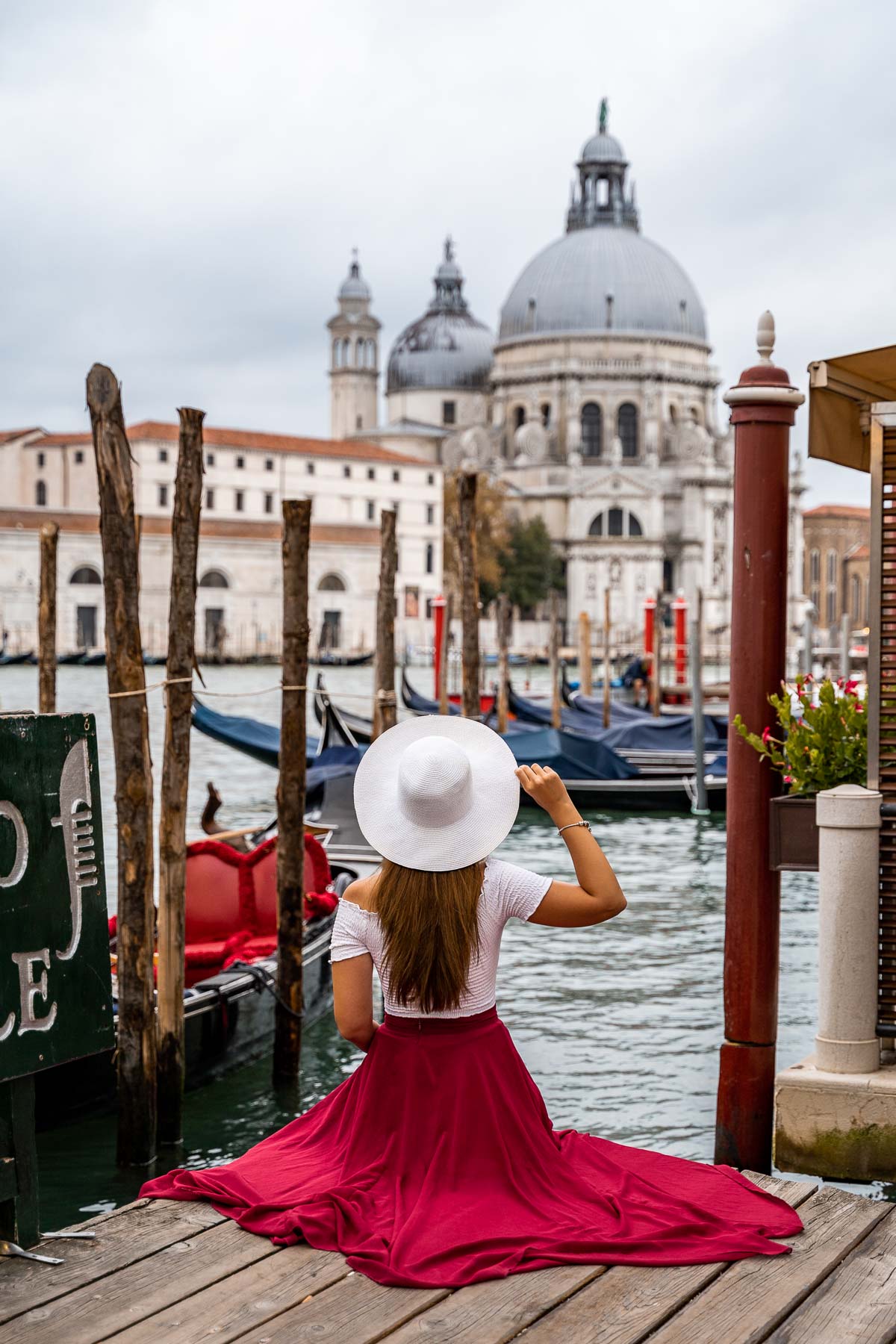 Girl in a red skirt sitting on a pier looking at Santa Maria della Salute in Venice, Italy