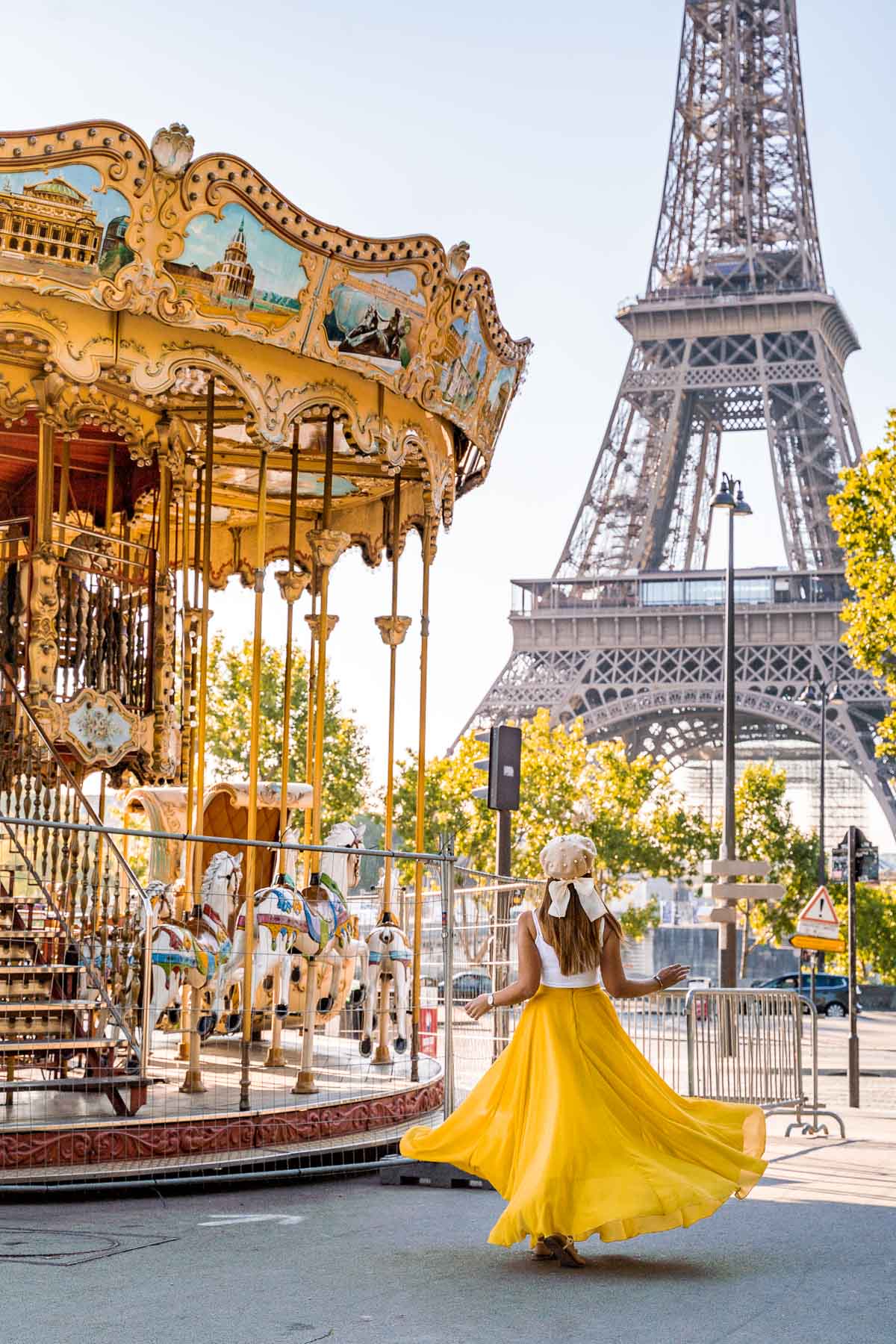 Girl in a yellow skirt twirling in front of a carousel near the Eiffel Tower in Paris