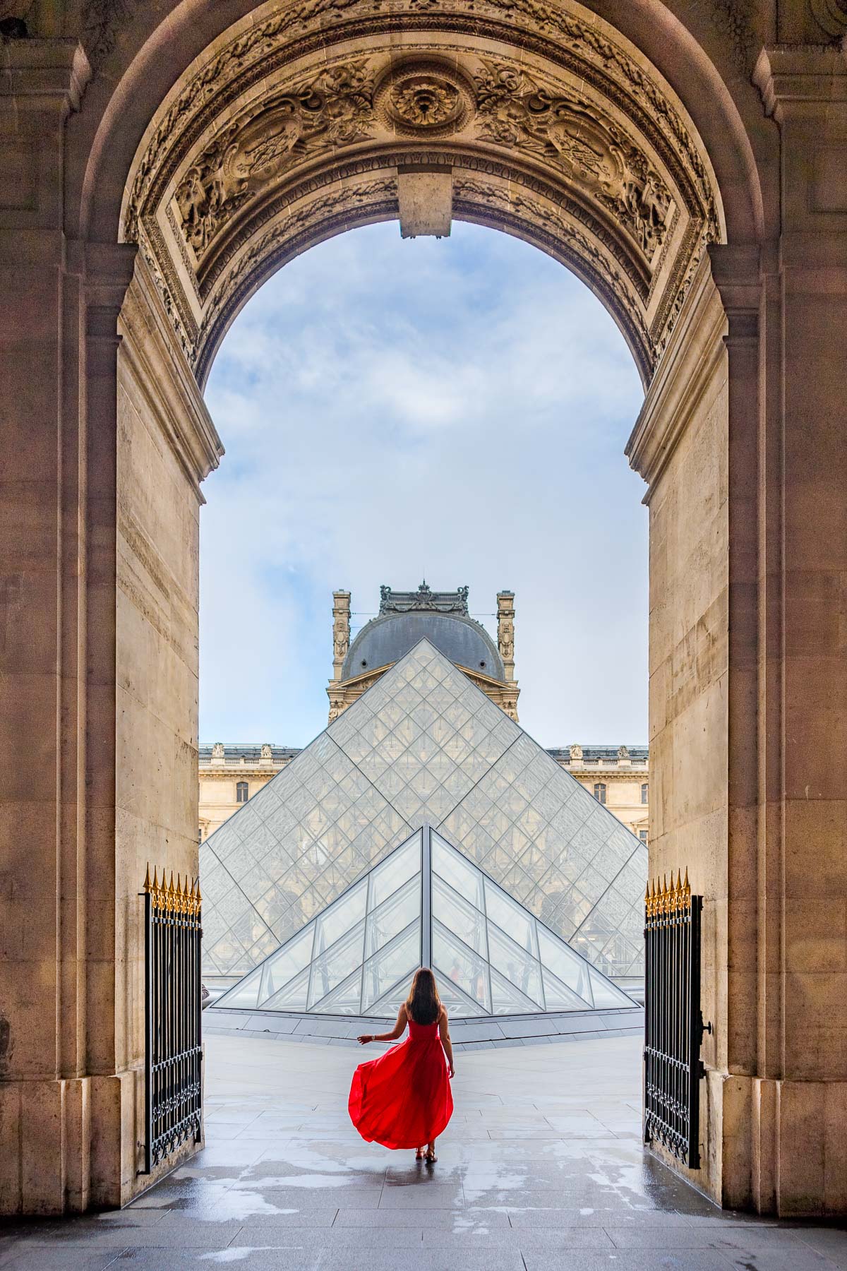 Girl in a red dress standing in front on the Louvre, one of the most Instagrammable places in Paris