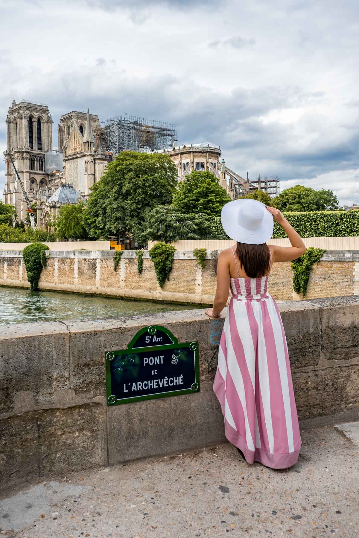 Girl in a pink-white dress standing on Pont L'Archevéche, looking at the Notre Dame in Paris