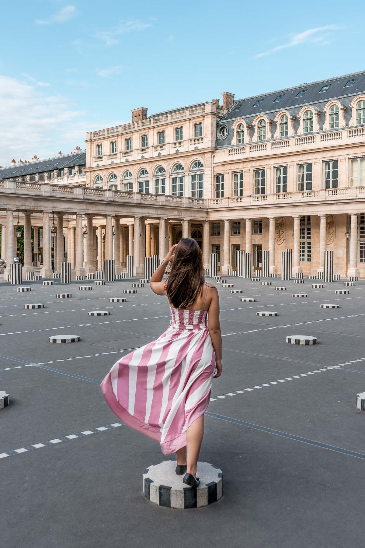 Girl in a pink-white striped dress standing in Palais Royal, one of the best Paris Instagram Spots