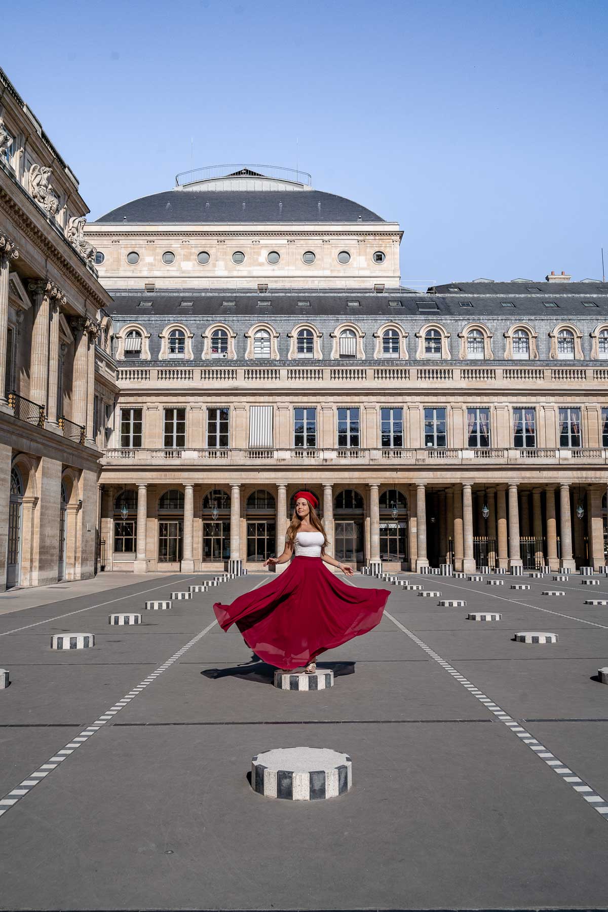 Girl in a red dress standing in Palais Royal, one of the most instagrammable places in Paris