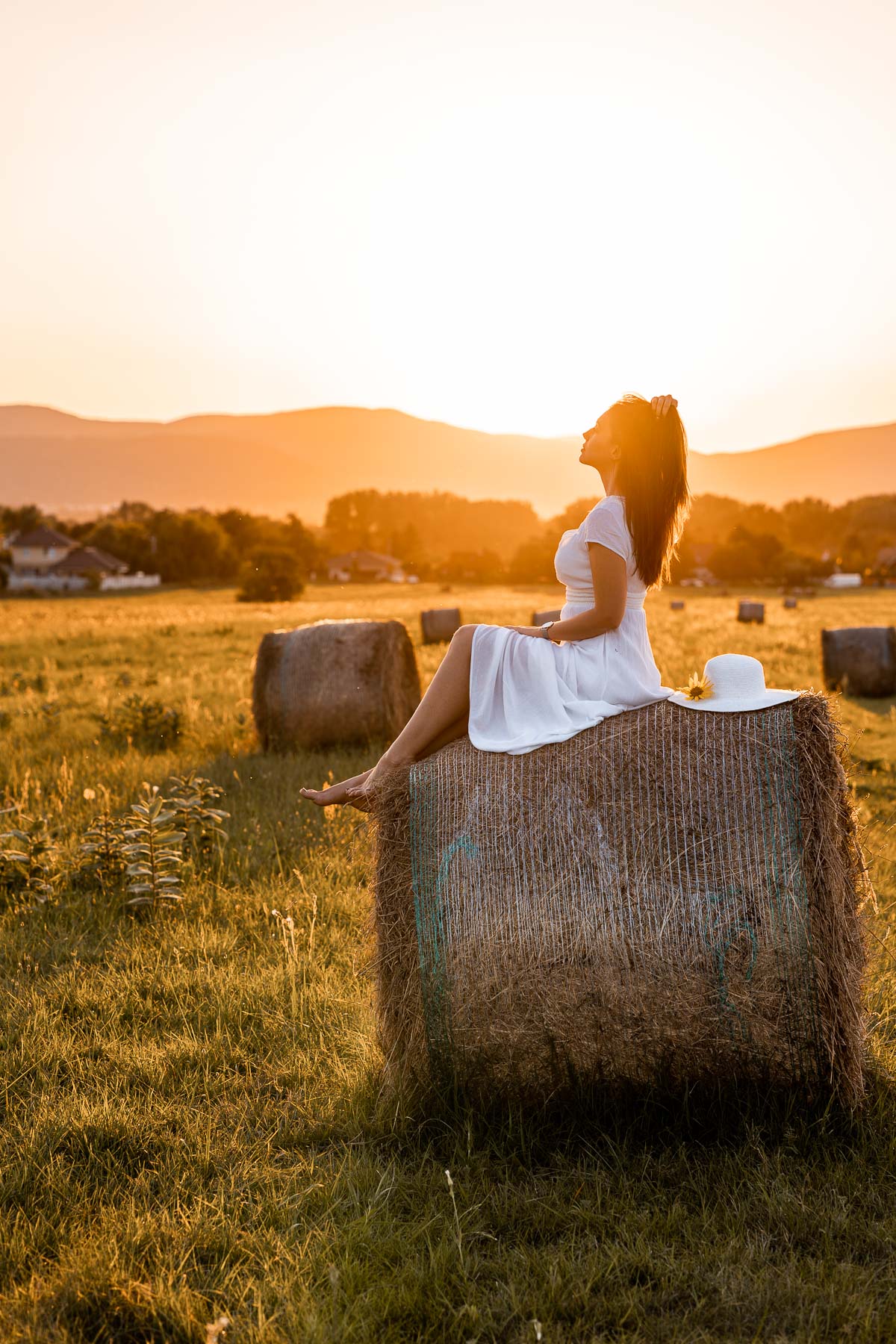 Girl in a white dress sitting on a haystack at sunset