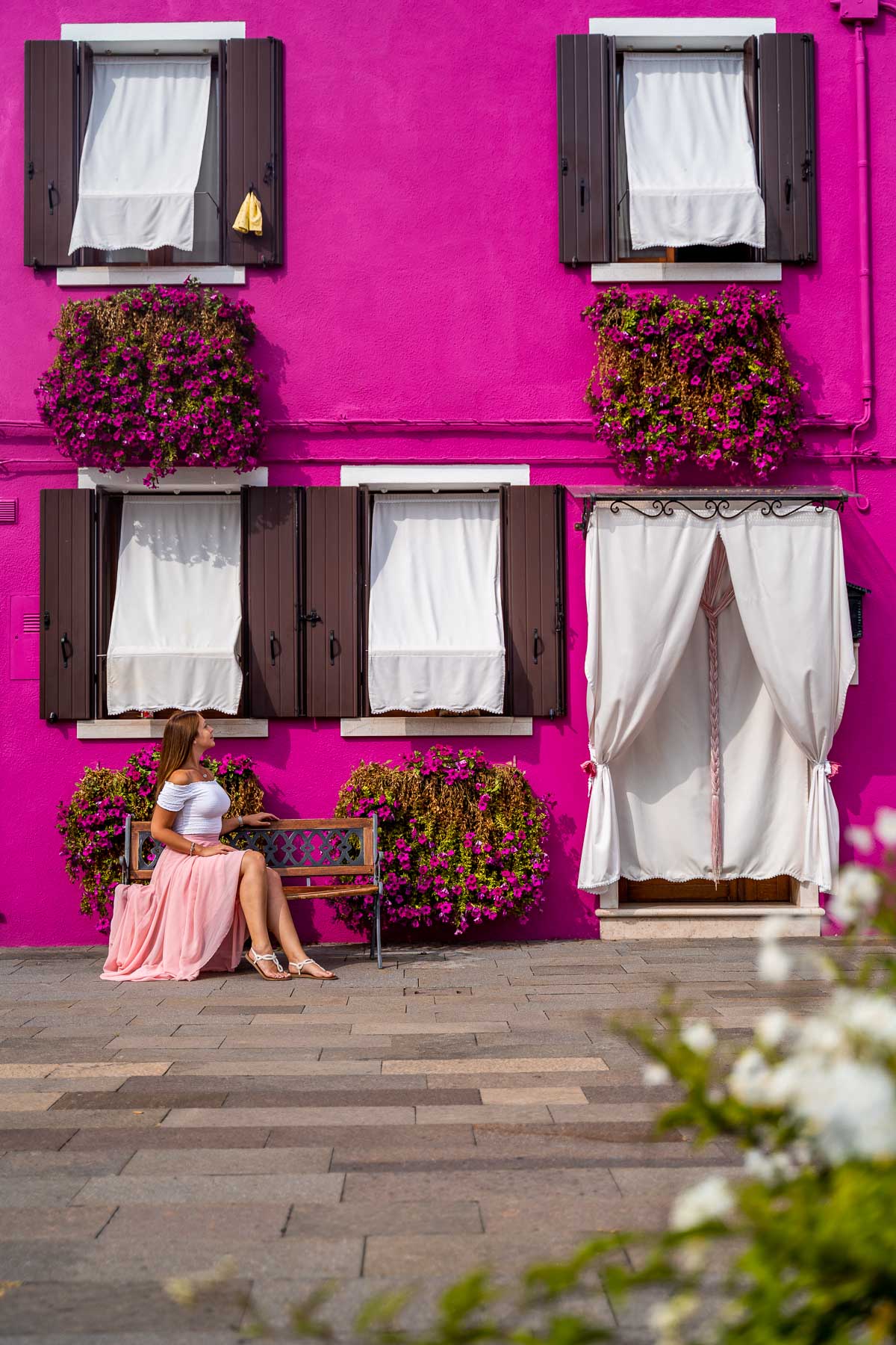 Girl in a pink skirt sitting in front of a pink house in Burano