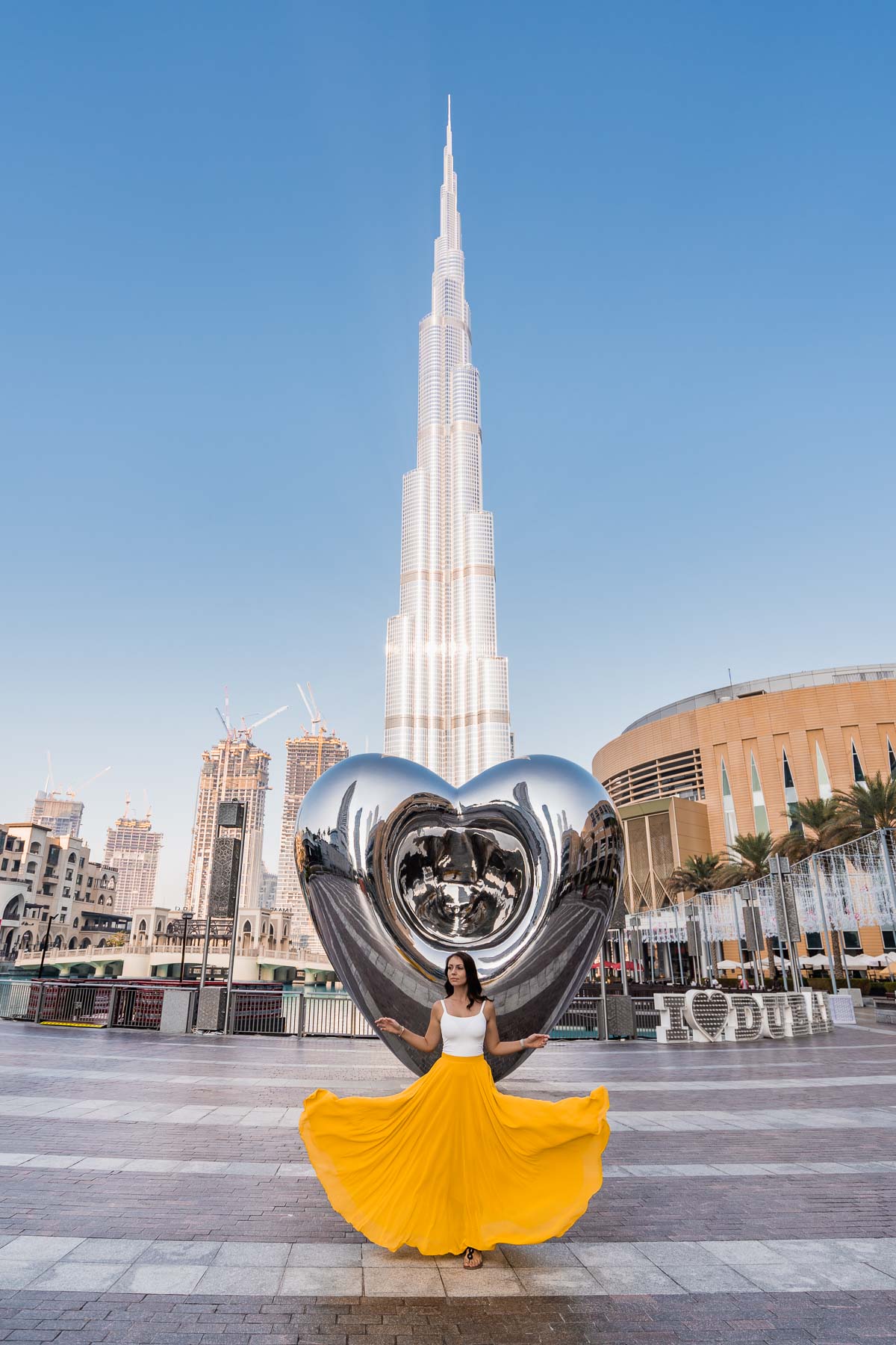 Girl in yellow skirt doing a skirt flip in front of the Dubai Steel Heart with the Burj Khalifa in the background