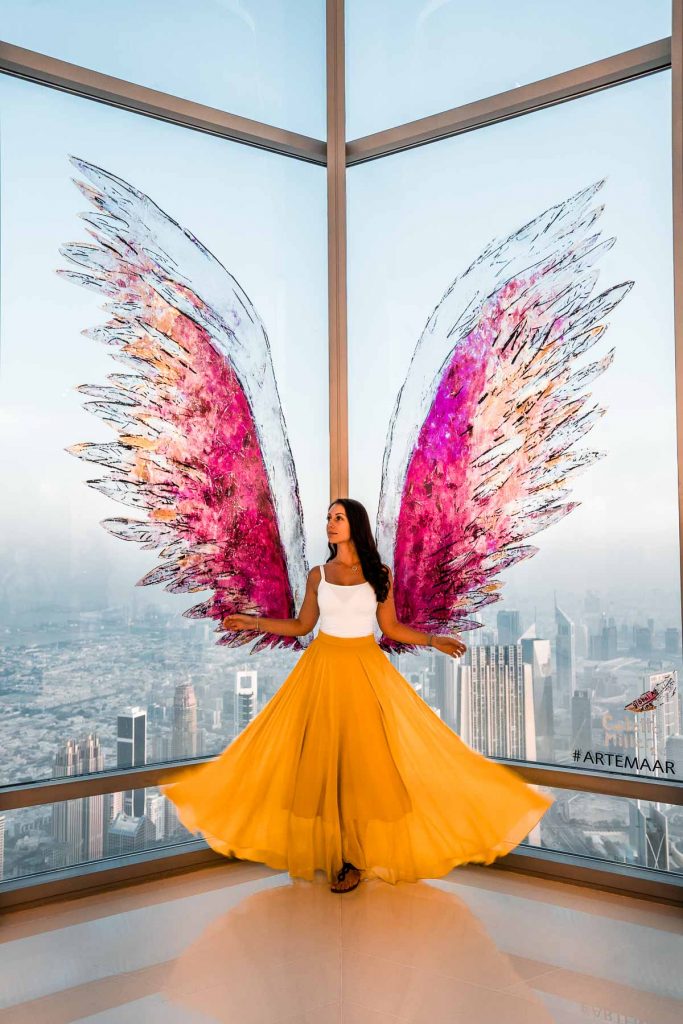 Girl in a yellow skirt standing in front of a pink instagrammable wing at the Burj Khalifa in Dubai