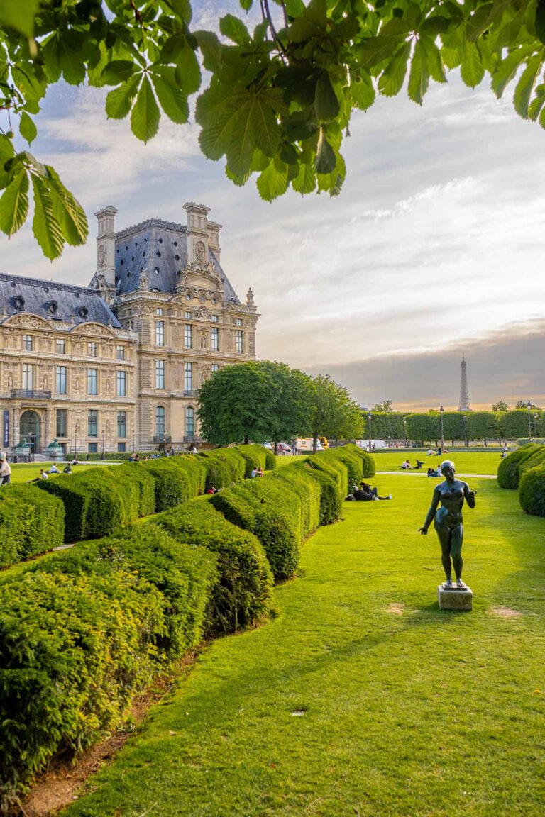 A peaceful spot in Jardin des Tuileries in Paris with tidy hedges, a statue, and the Eiffel Tower peeking out in the distance under a soft, golden sky.