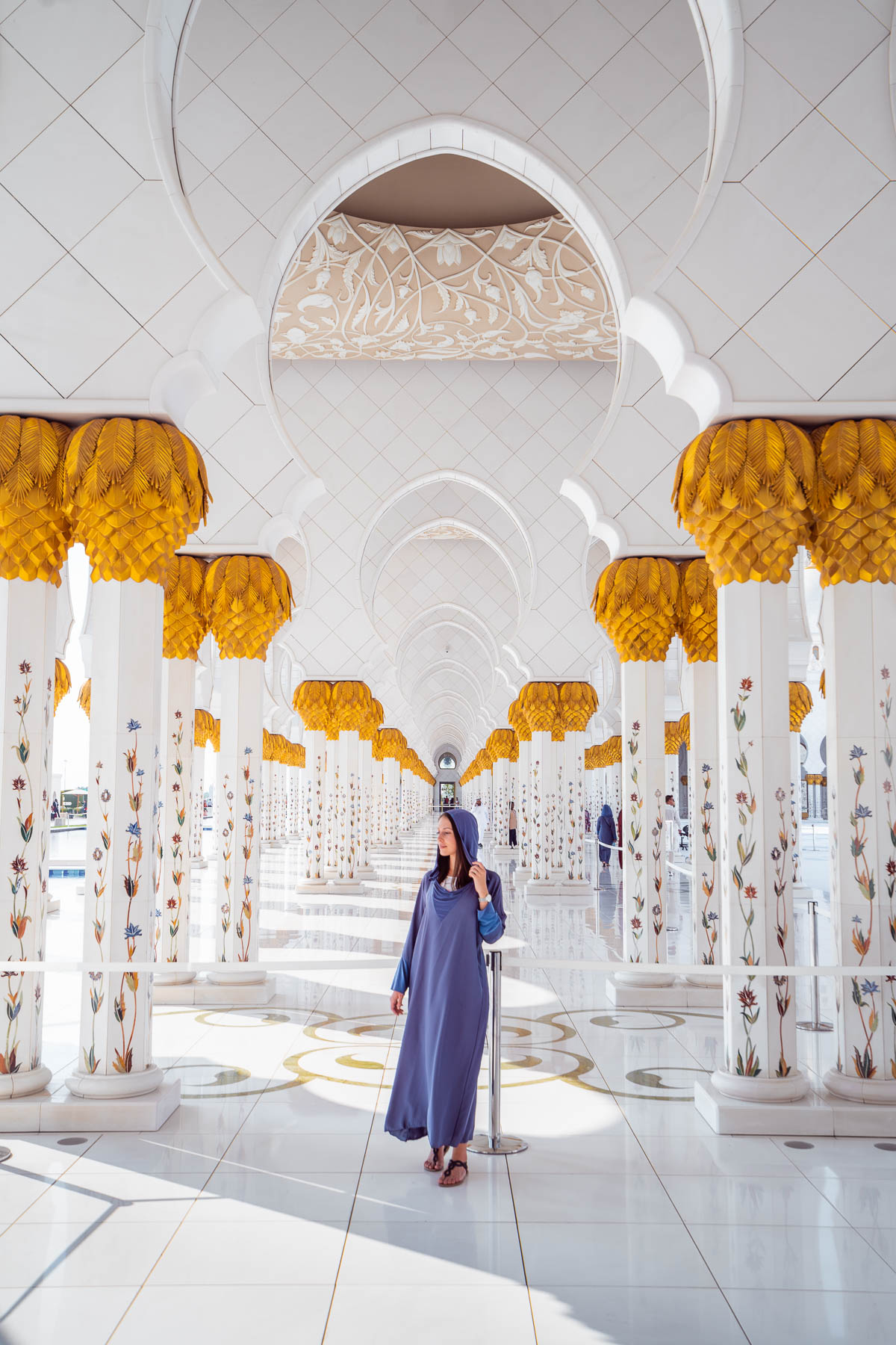 Girl in a blue abaya standing between the gold-white columns in Sheikh Zayed Grand Mosque, Abu Dhabi