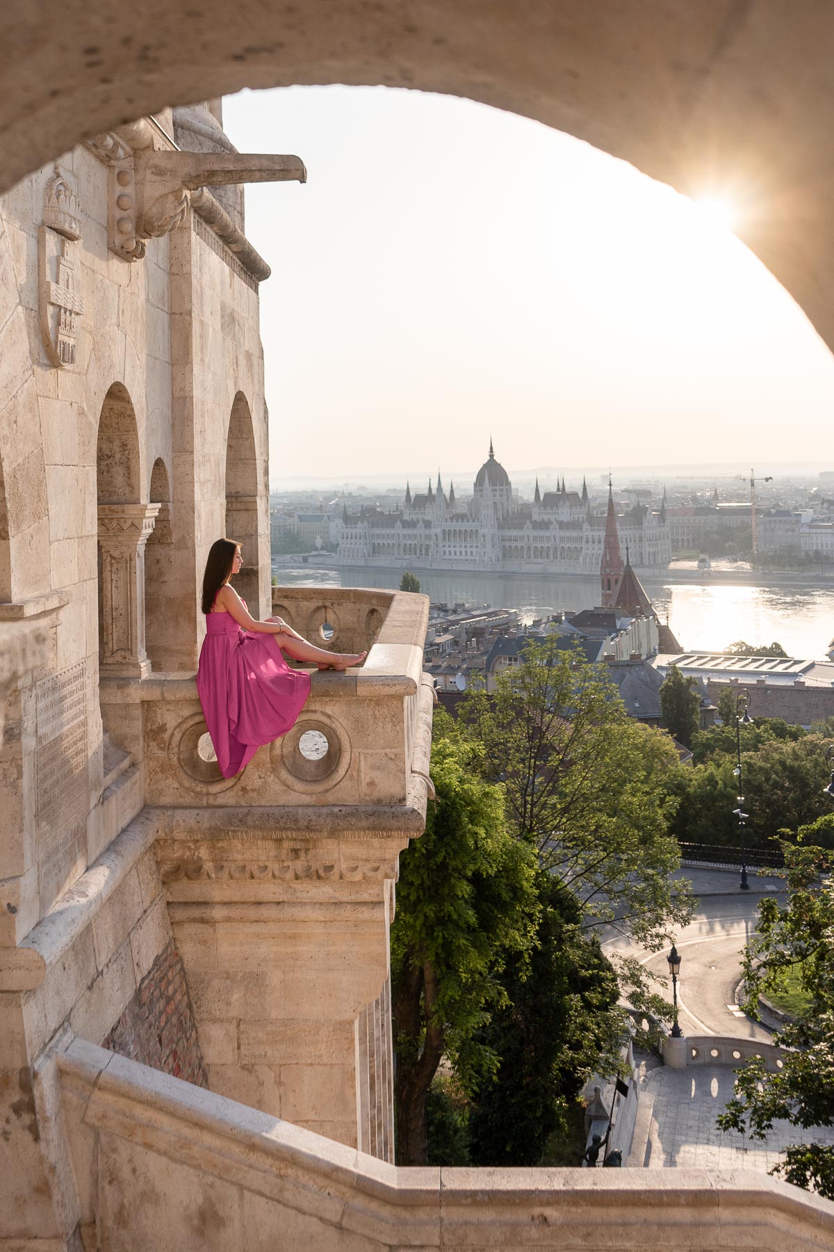 Girl in pink dress sitting at the edge of the Fisherman's Bastion in Budapest with the Hungarian Parliament in the background
