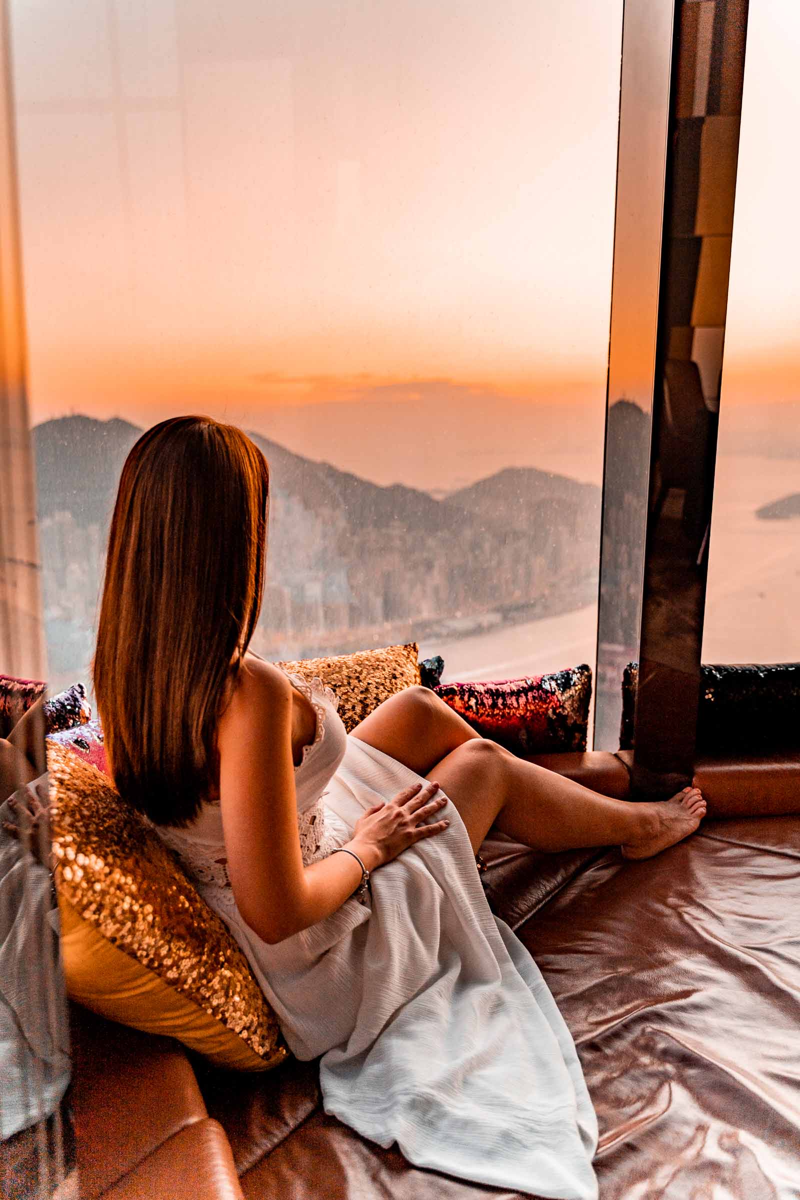 Girl in a white dress looking at the sunset from the highest bar in the world in Hong Kong