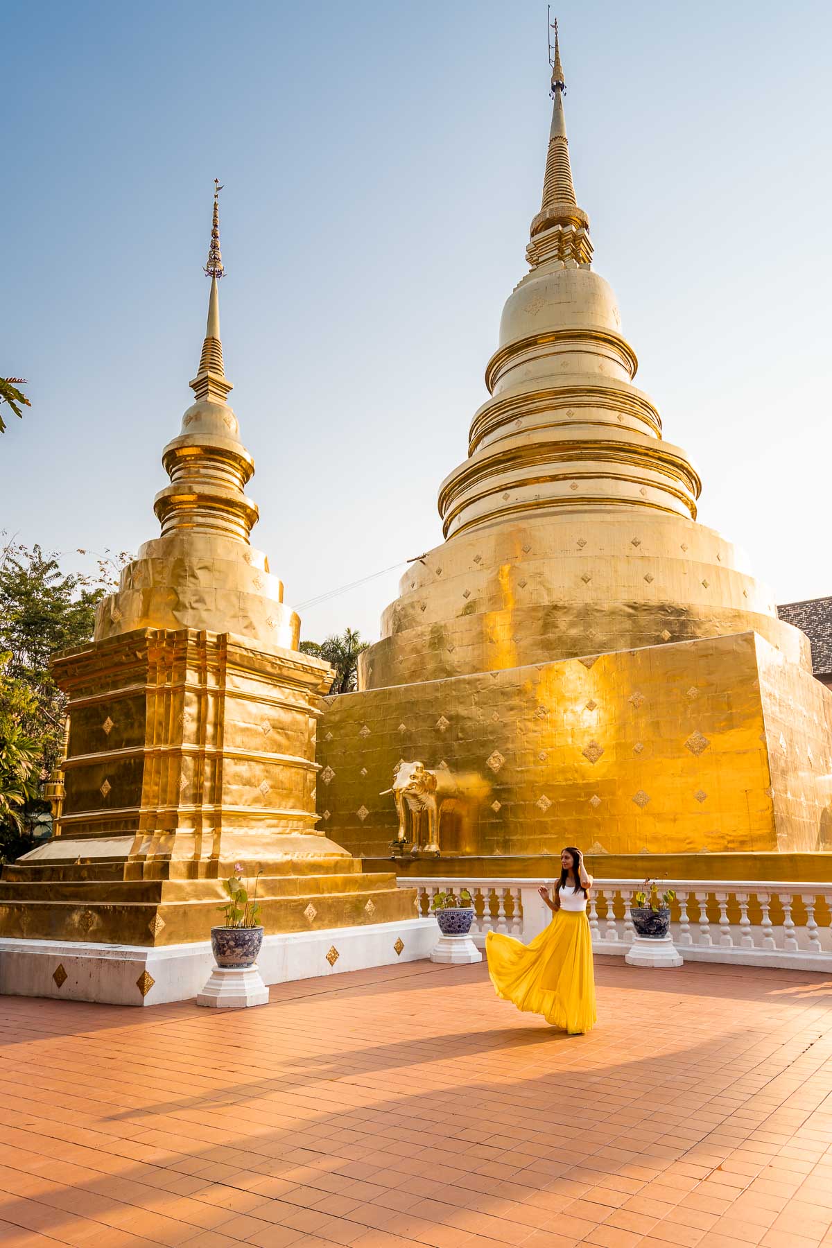 Girl in a yellow skirt in front of the golden stupas at Wat Phra Singh Temple in Chiang Mai