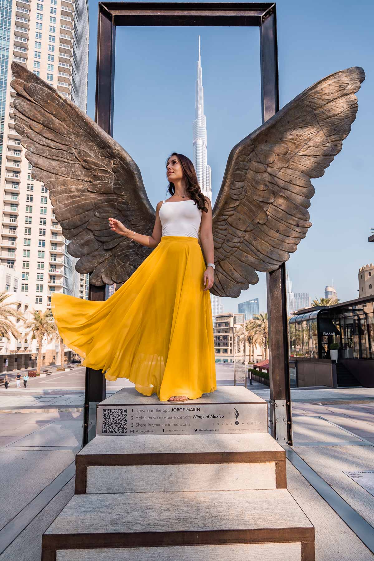Girl in yellow skirt doing a skirt flip in front of the Wings of Mexico in Dubai with the Burj Khalifa in the background