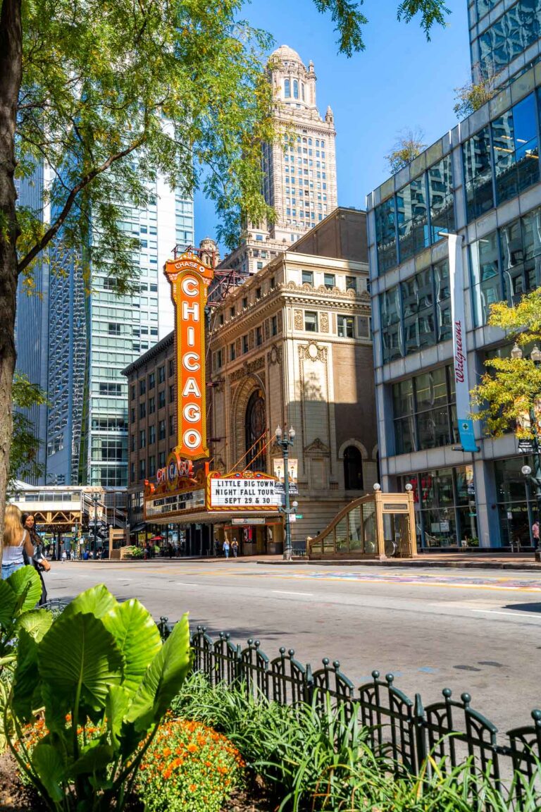 A city view of the Chicago Theater with its famous red sign, surrounded by tall buildings and greenery in the foreground.