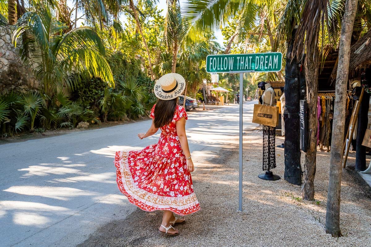 Girl in red dress next to the famous Follow That Dream sign in Tulum