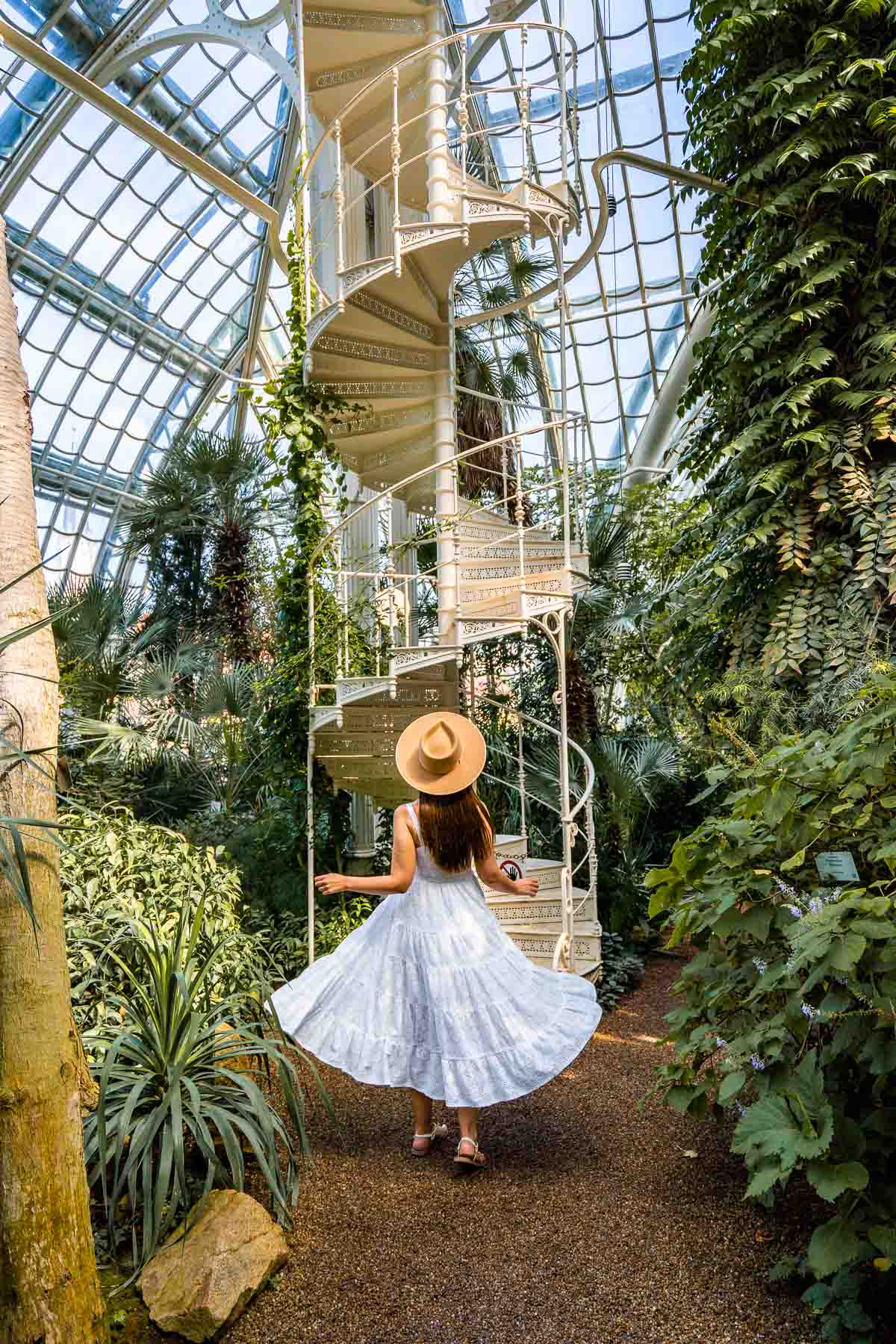 Girl in a white dress in front of a white spiral staircase inside Palmenhaus Schönbrunn