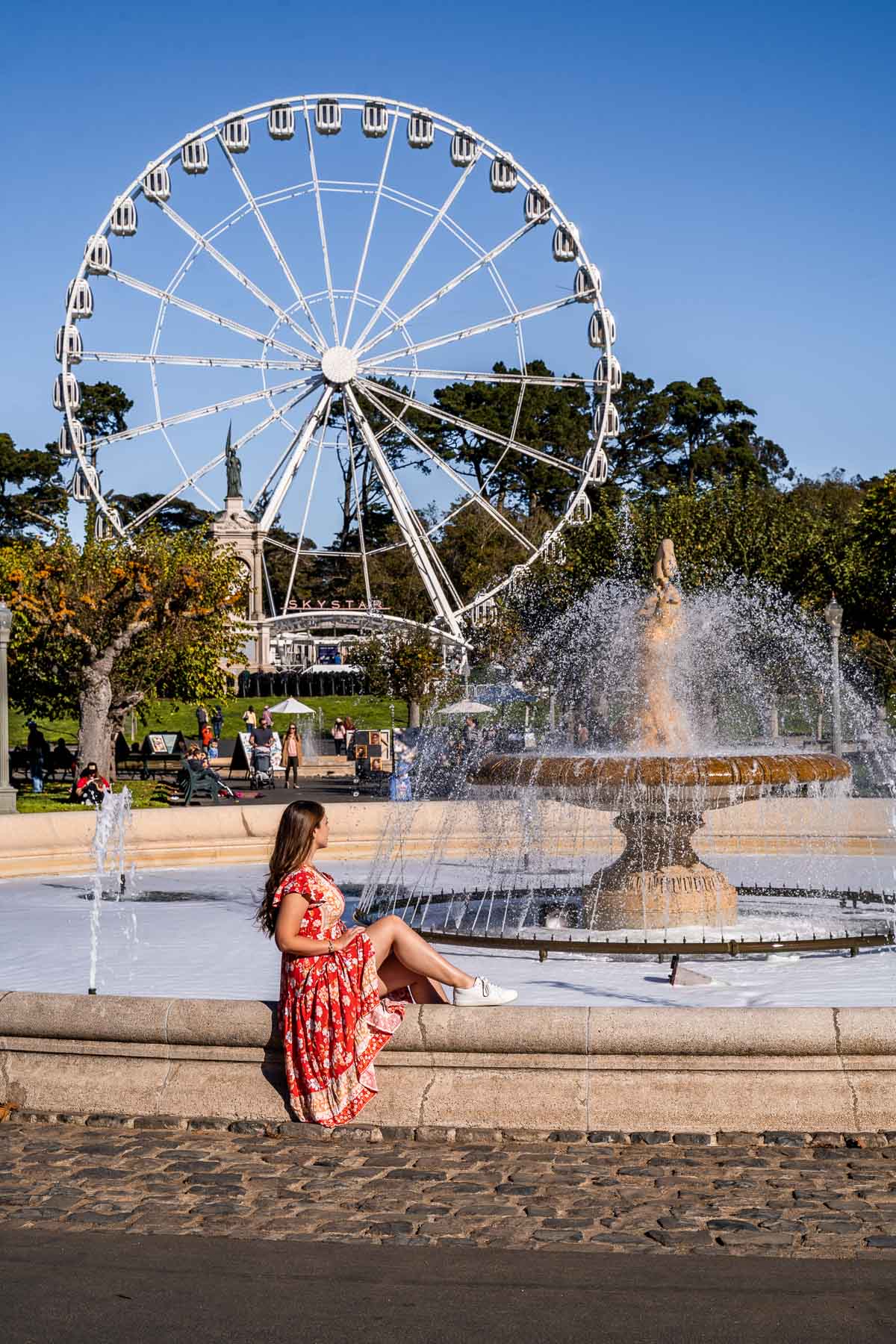 Girl sitting on a fountain in front of SkyStar Wheel in San Francisco
