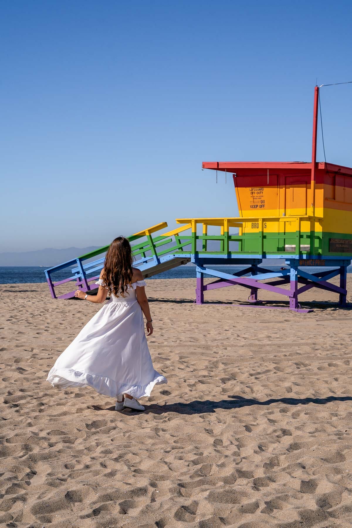 Girl in white dress in front of the Venice Pride Flag Lifeguard Tower, Los Angeles