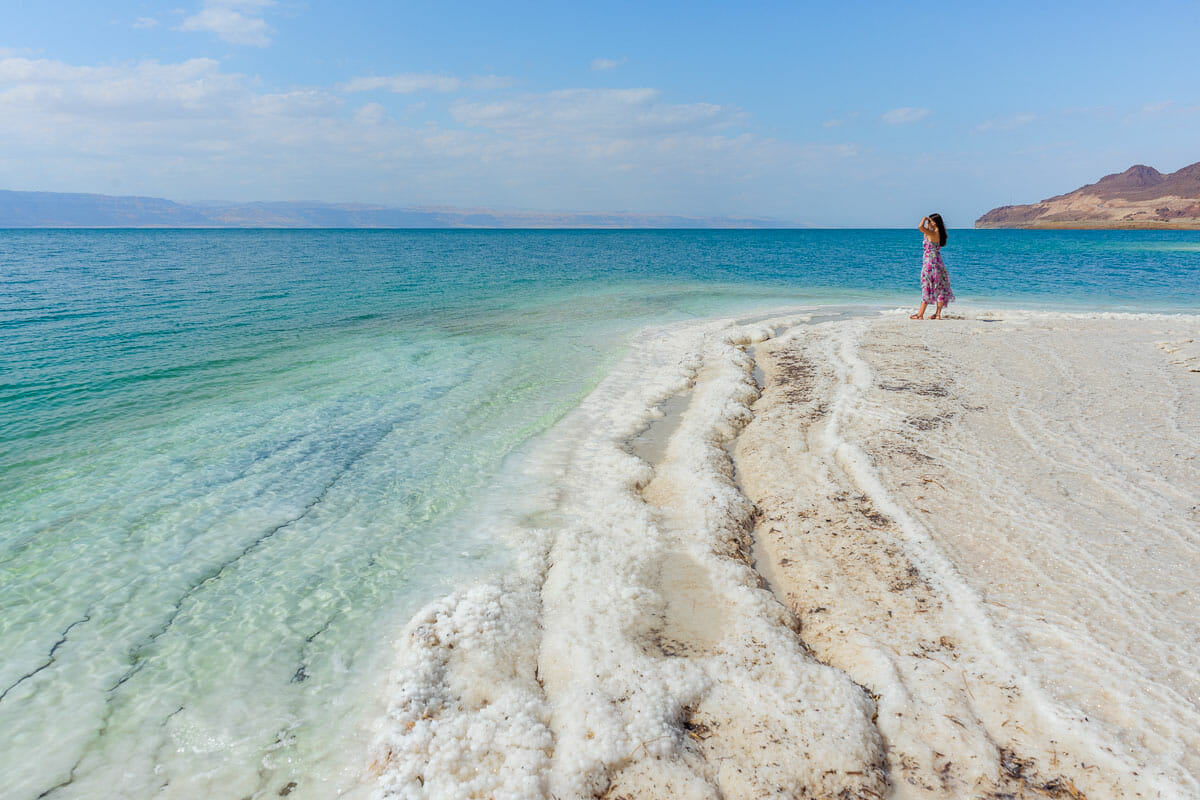 Girl in a pink floral dress standing on the white salt formations at the Dead Sea in Jordan