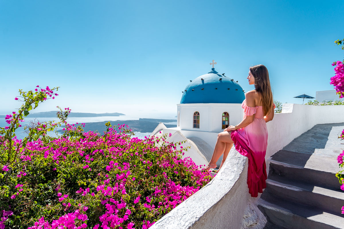 Girl sitting in front of a blue domed church in Imerovigli, Santorini
