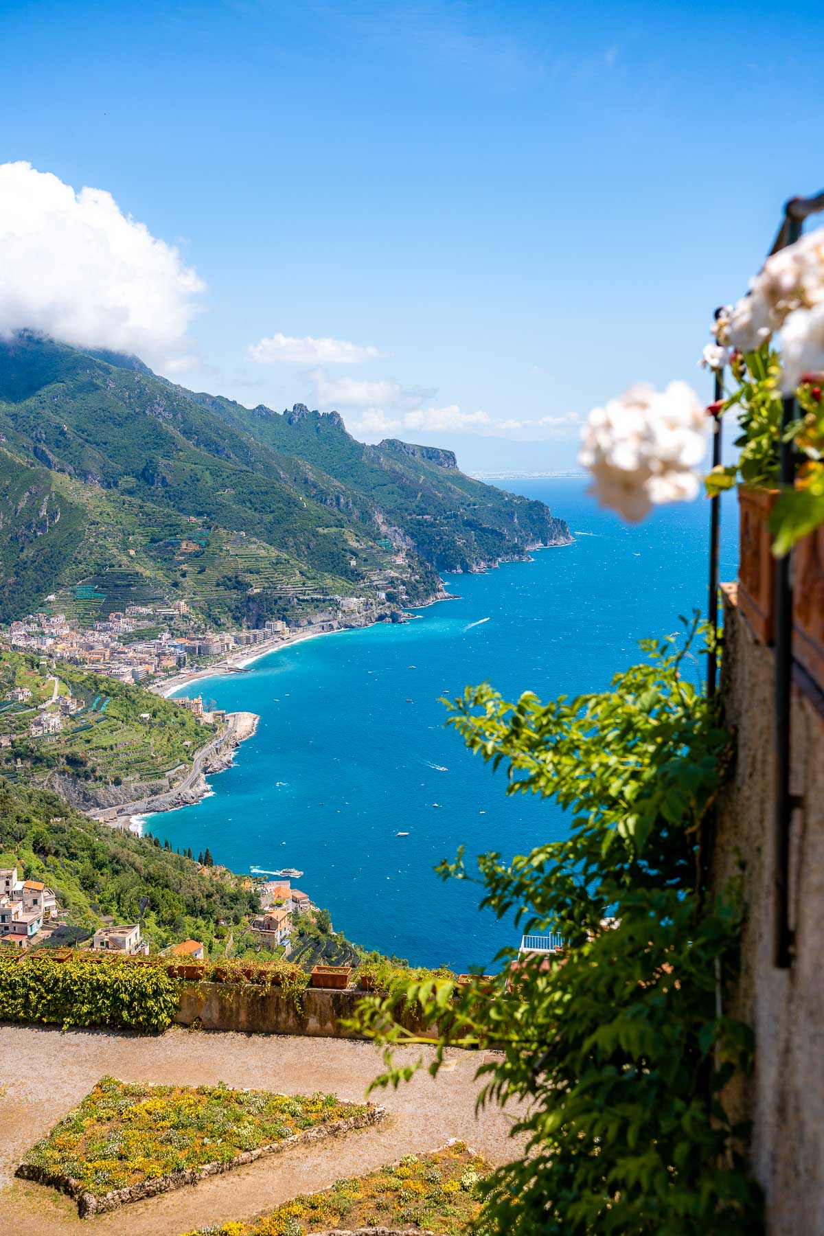 A view of the coastline from Villa Rufolo in Ravello, Italy. The blue sea stretches along the cliffs, with greenery and flowers in the foreground.