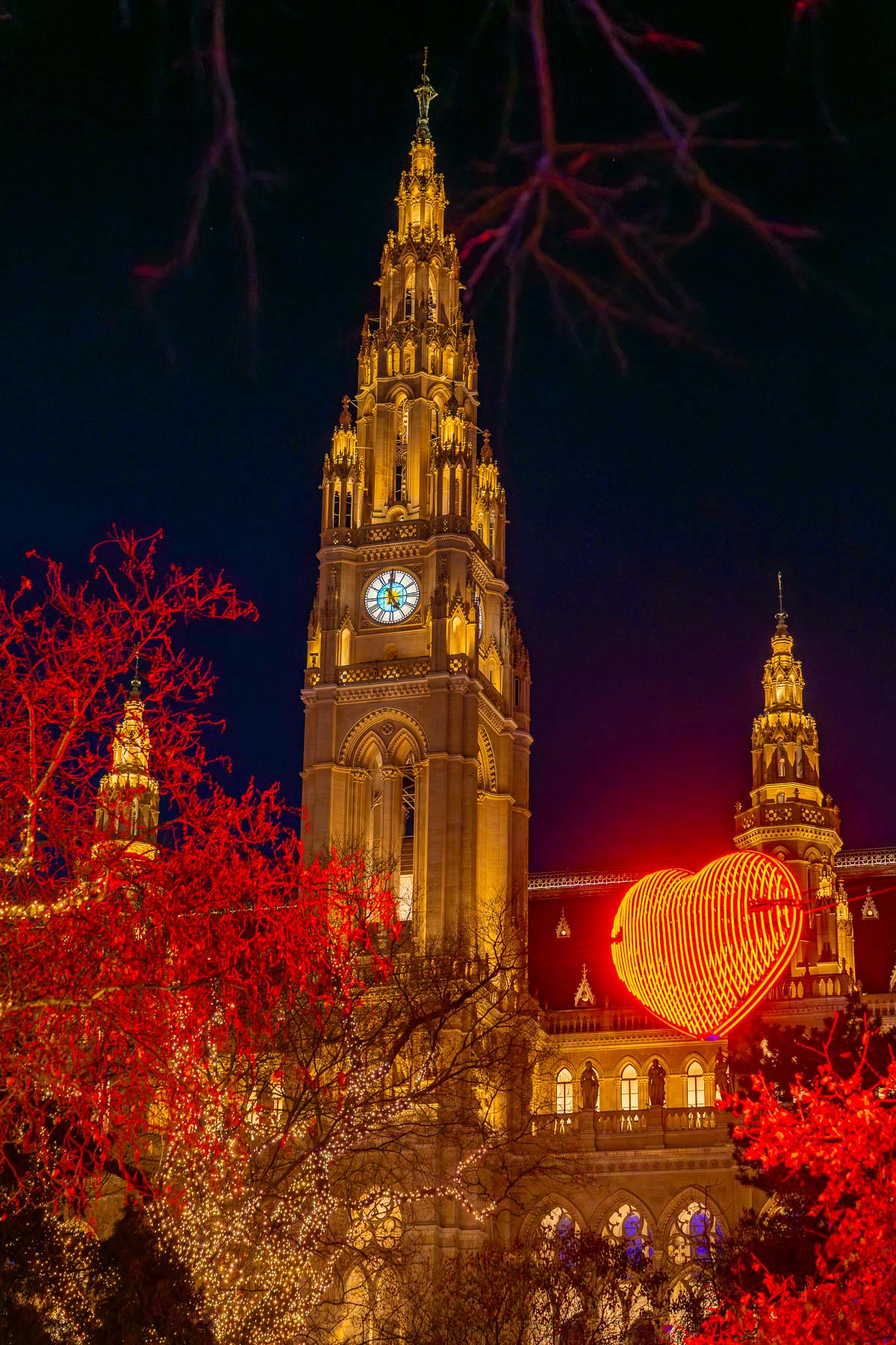 Vienna City Hall lit up at night with a large red heart light display and glowing trees at the Rathausplatz Christmas market.