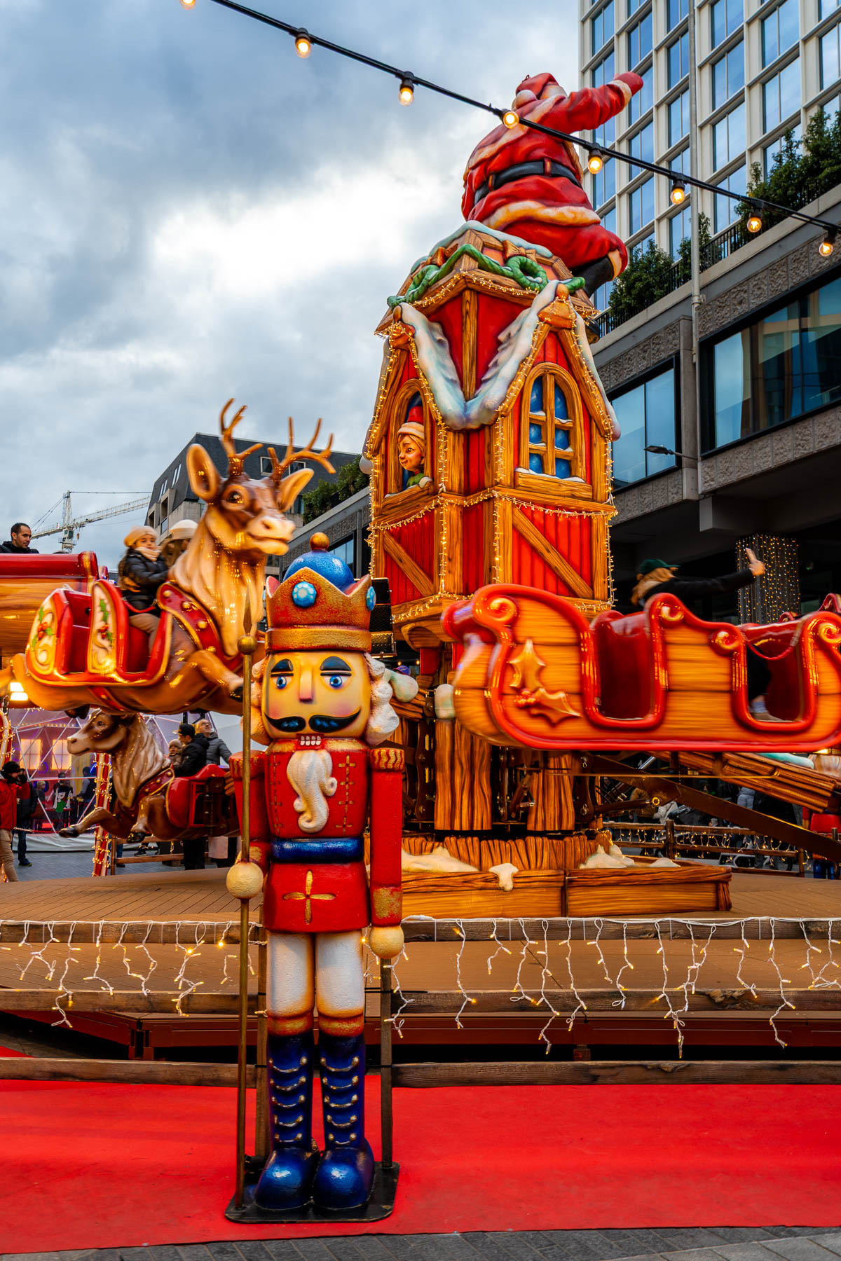 Festive ride with reindeer, sleighs, and a large nutcracker figure at the Brussels Christmas market, with string lights and people enjoying the scene.