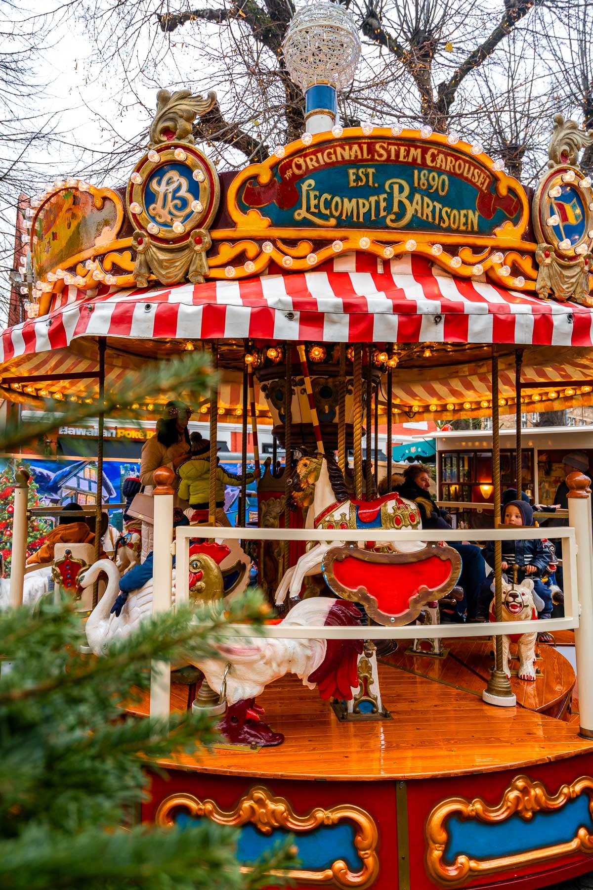 Children riding a colorful vintage carousel at the Christmas market on Simon Stevinplein in Bruges.