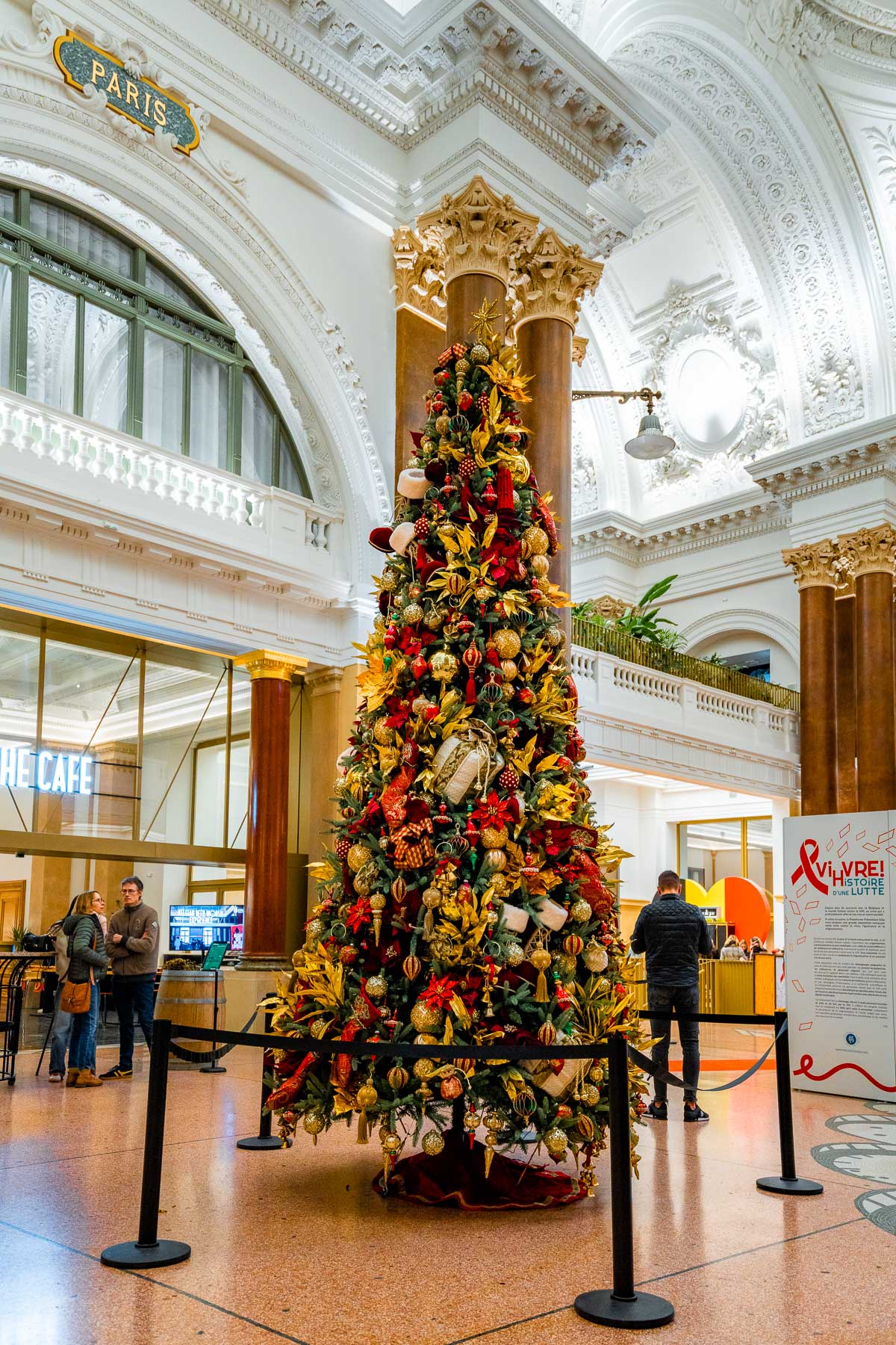 Beautifully decorated Christmas tree inside the Brussels Stock Exchange, surrounded by ornate architecture and festive gold and red ornaments.