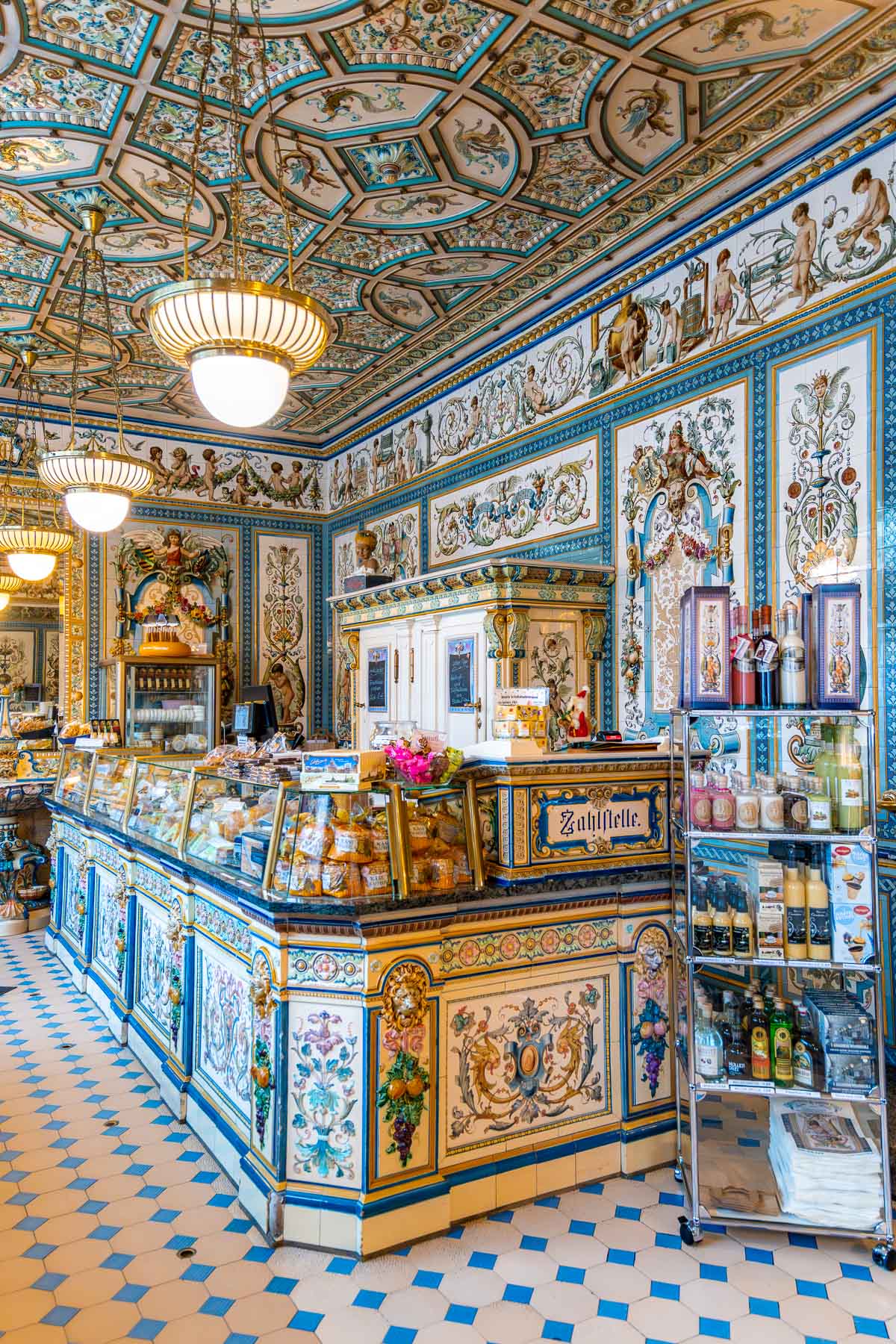 Interior of Dresdner Molkerei Gebrüder Pfund with ornate painted tiles, intricate patterns, and a colorful counter filled with dairy products and local goods.
