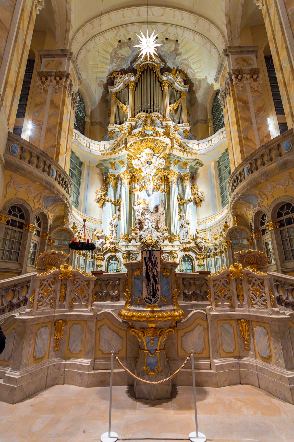 The ornate altar and pipe organ inside the Frauenkirche in Dresden, beautifully decorated with gold details and a glowing star hanging above.