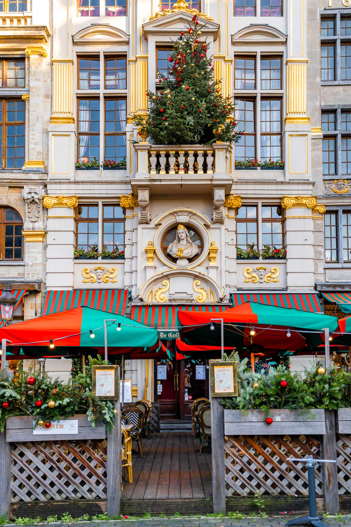 Restaurant in Brussels’ Grand Place decorated for Christmas with red and green awnings, garlands, and a Christmas tree on the balcony above the entrance.