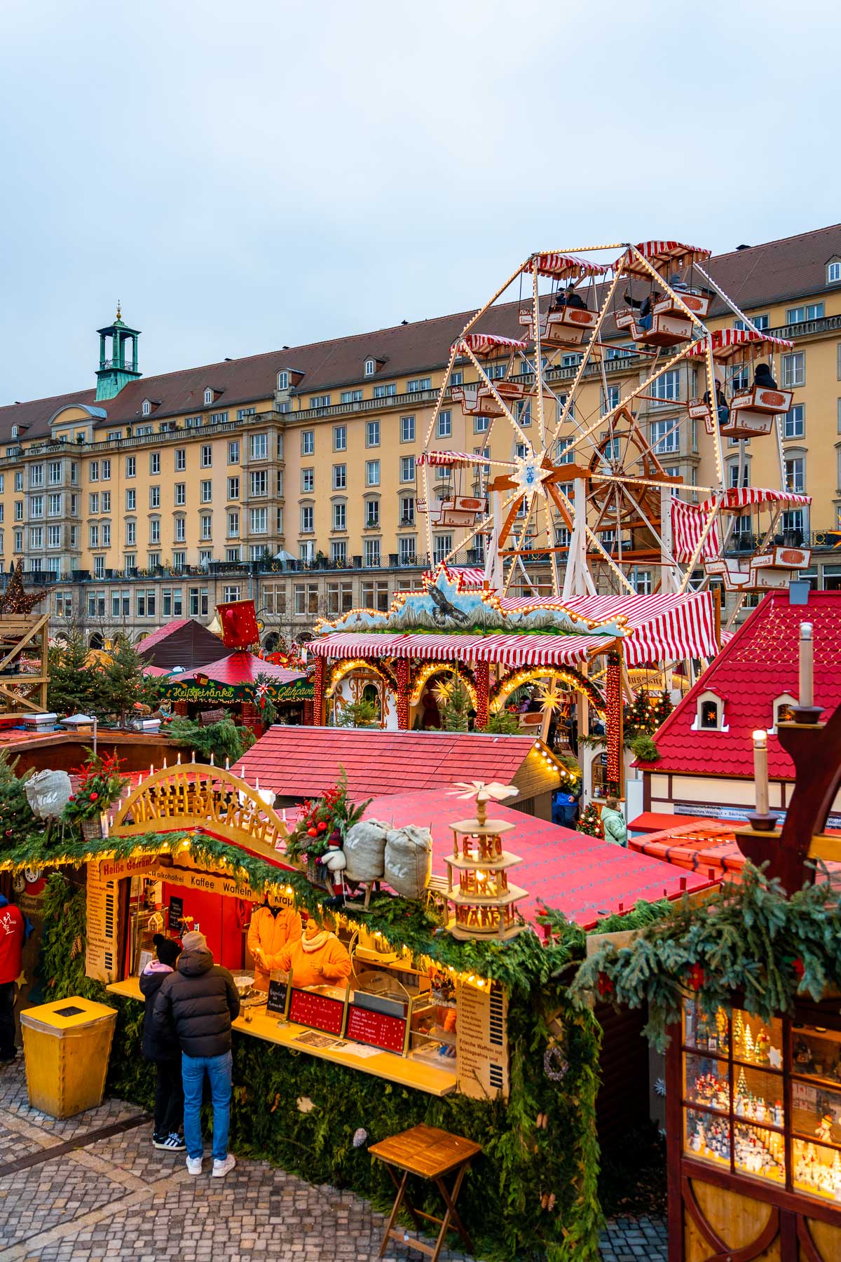 View of the Striezelmarkt in Dresden showing the Ferris wheel, festive stalls, and Christmas decorations in front of the city’s historic buildings.