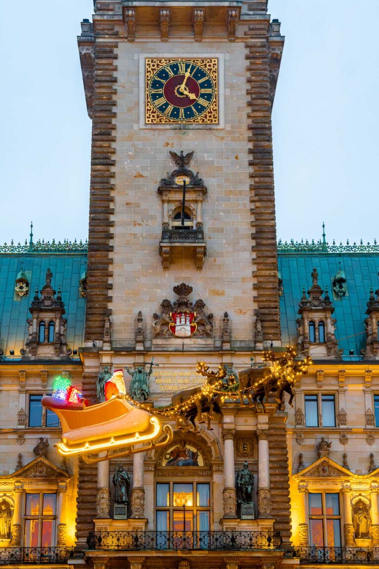 Front view of Hamburg City Hall at the Christmas Market at Rathausmarkt, with a fyling Santa sleigh and reindeer decoration suspended in front of the building.