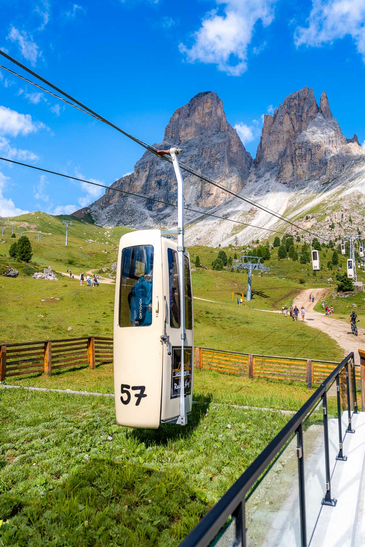 The coffin cable car at Forcella del Sassolungo in the Dolomites with rugged mountain peaks rising behind the lift and alpine meadows below.