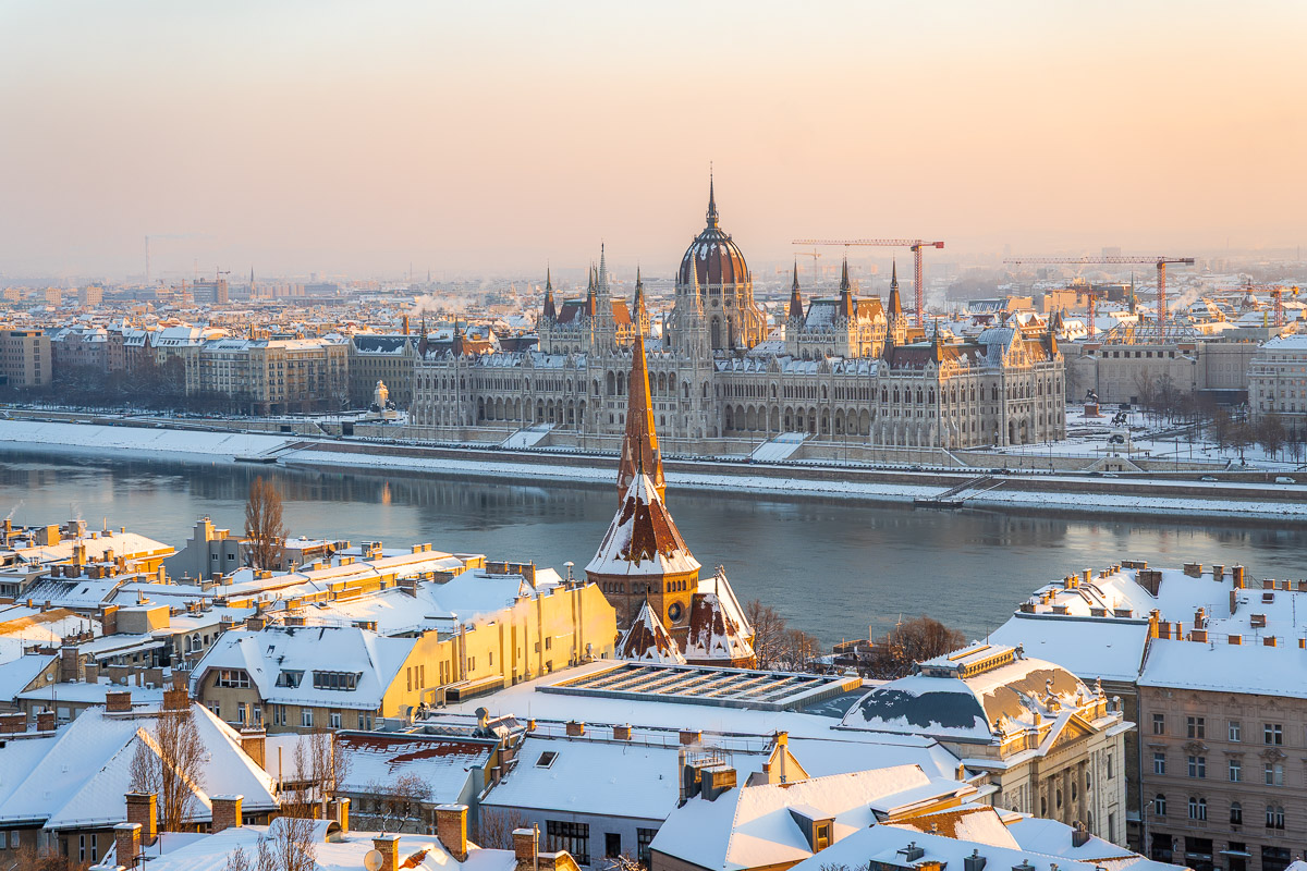 View from Fisherman’s Bastion in Budapest looking over snow covered rooftops, with the Danube River and the Hungarian Parliament building in the background.