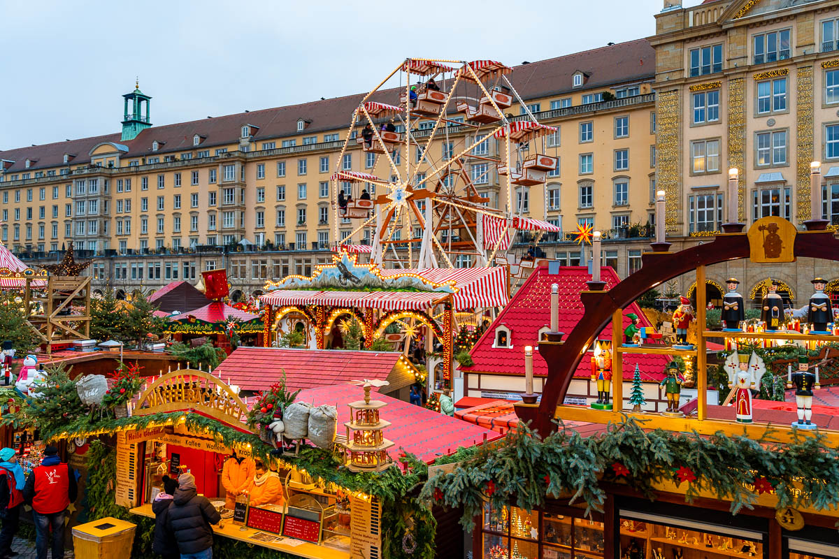 View of the Striezelmarkt in Dresden showing the Ferris wheel, festive stalls, and Christmas decorations in front of the city’s historic buildings.