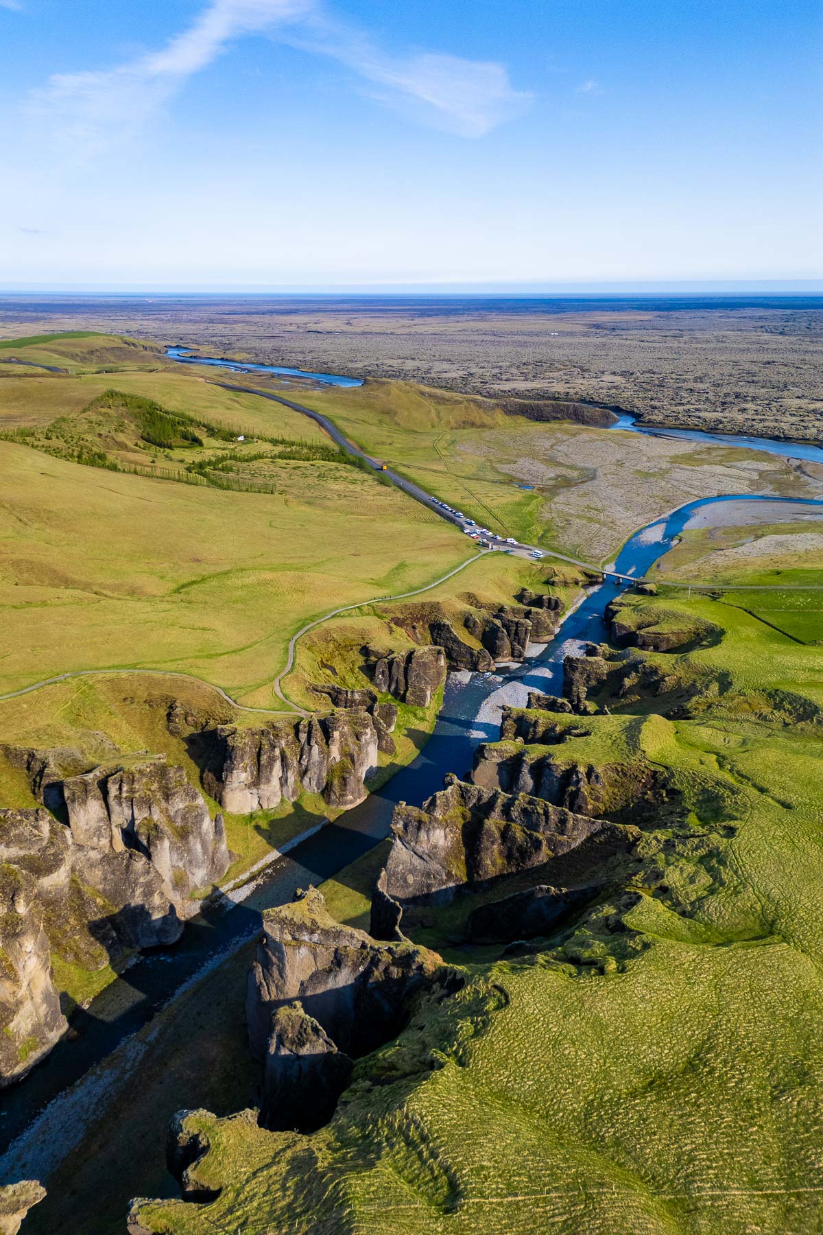 An aerial view of Fjadrargljufur Canyon, Iceland shows a winding river cutting through steep green cliffs and open fields.