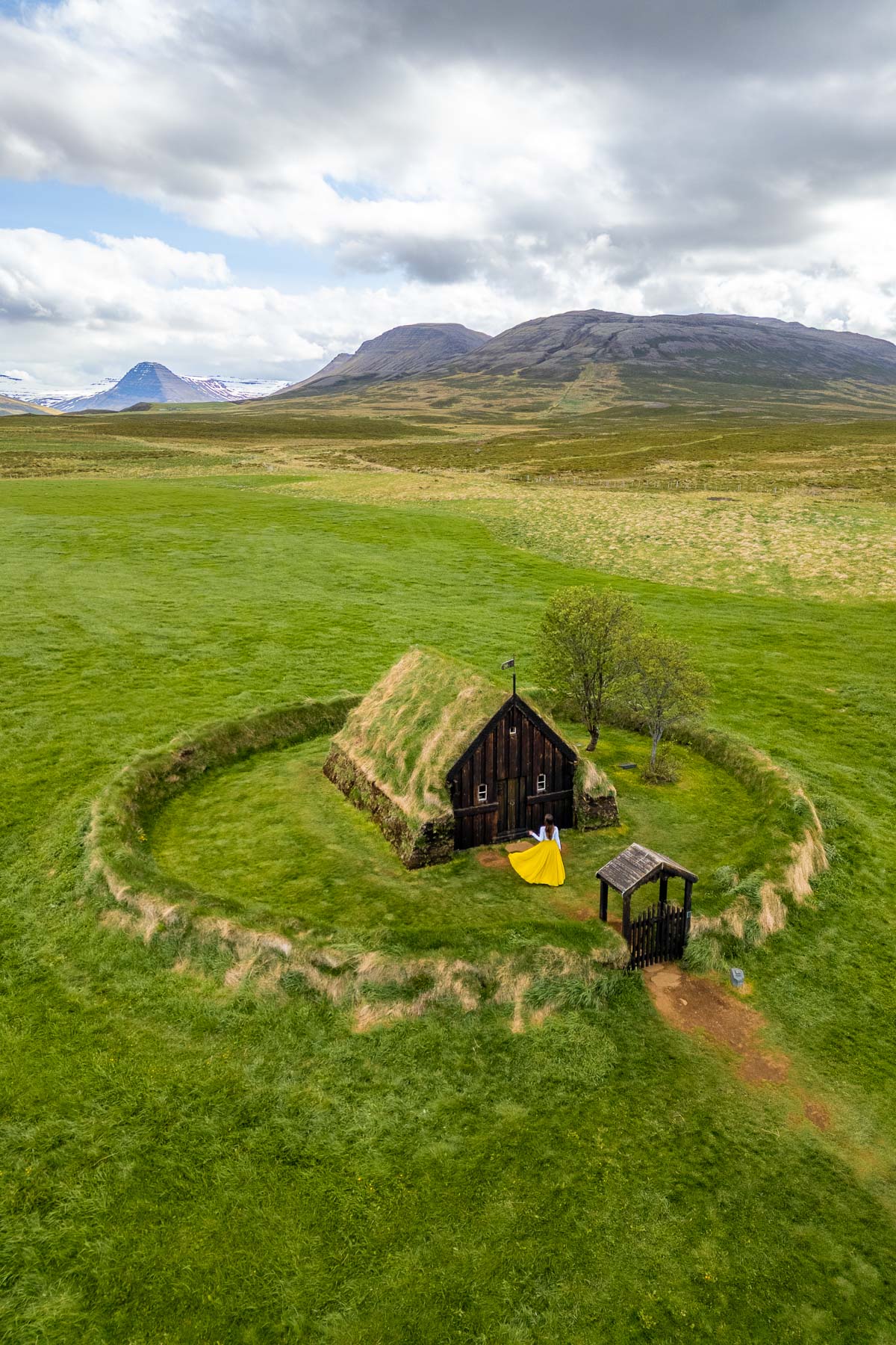 A small turf church at Grafarkirkja, Iceland sits in the middle of a circular grass enclosure with mountains and open fields in the background.